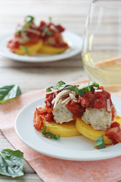 A white plate with Ground Turkey Meatballs and polenta cakes with wine in the background.