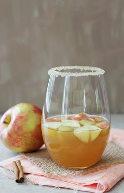 A glass of Apple Cider Sangria with a fresh apple and cinnamon stick to the side.