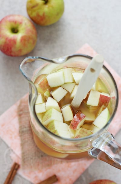 A glass pitcher filled with Fall Sangria with fresh chopped apples.