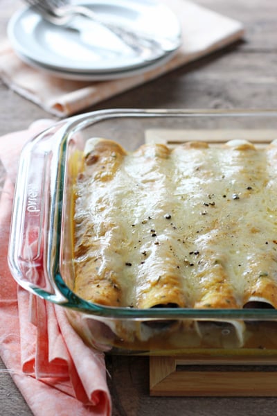 A glass baking dish with Sausage Enchiladas and plates in the background.