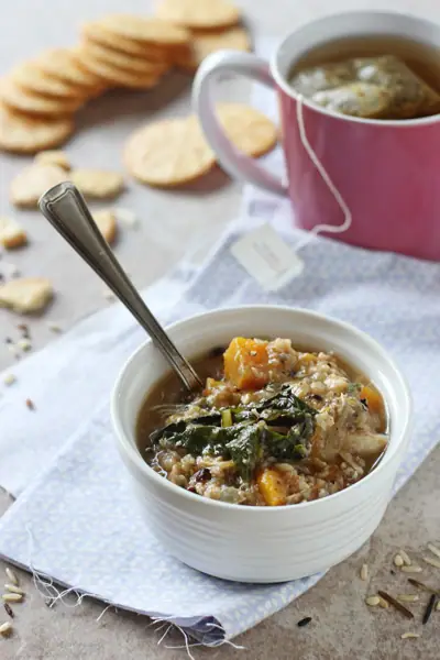 A bowl of Crockpot Chicken Wild Rice Soup with crackers and tea in the background.