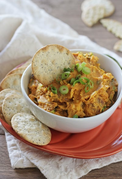 A white bowl filled with Savory Pumpkin Dip with a cracker in the bowl.