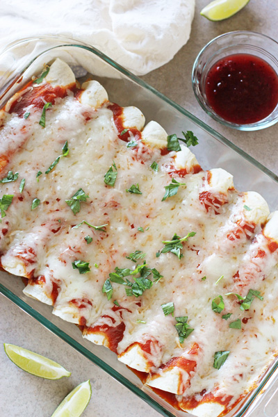 A baking dish filled with Leftover Turkey and Cranberry Enchiladas with a bowl of cranberry sauce to the side.