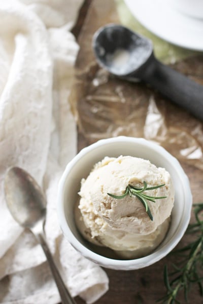 A white bowl of Rosemary Ice Cream with a scooper to the side.