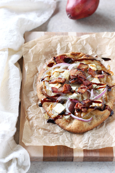 A Bacon, Brie and Pear Flatbread on a wooden cutting board.