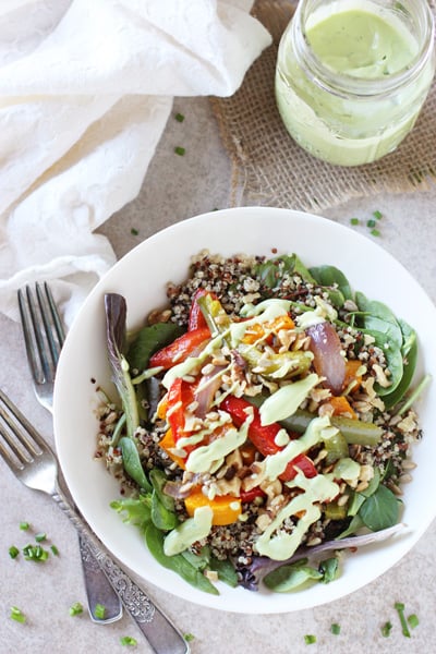 A white bowl filled with Roasted Vegetable Quinoa Salad with dressing in a jar to the side.