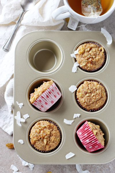 A muffin tin with several Healthy Morning Glory Muffins and a cup of tea.