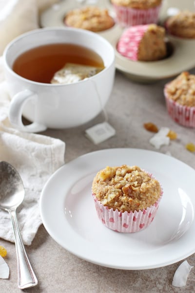 A Healthy Morning Glory Muffin on a white plate with a cup of tea to the side.