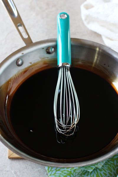 A skillet filled with DIY Balsamic Glaze with a whisk in the pan.