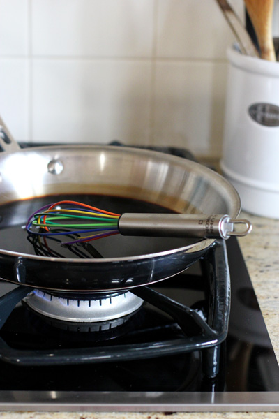 A skillet on a stovetop filled with balsamic vinegar and a whisk.