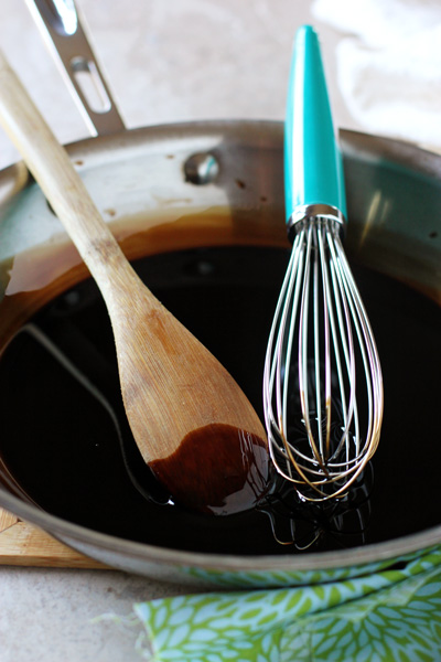 A skillet filled with Balsamic Reduction Sauce with a wooden spoon and whisk in the pan.