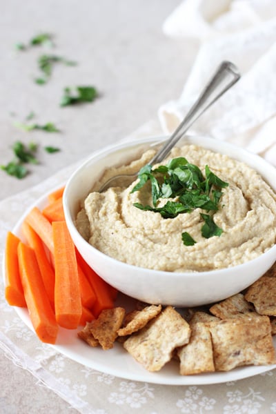 A serving dish filled with Chipotle Hummus and sliced carrots plus crackers.