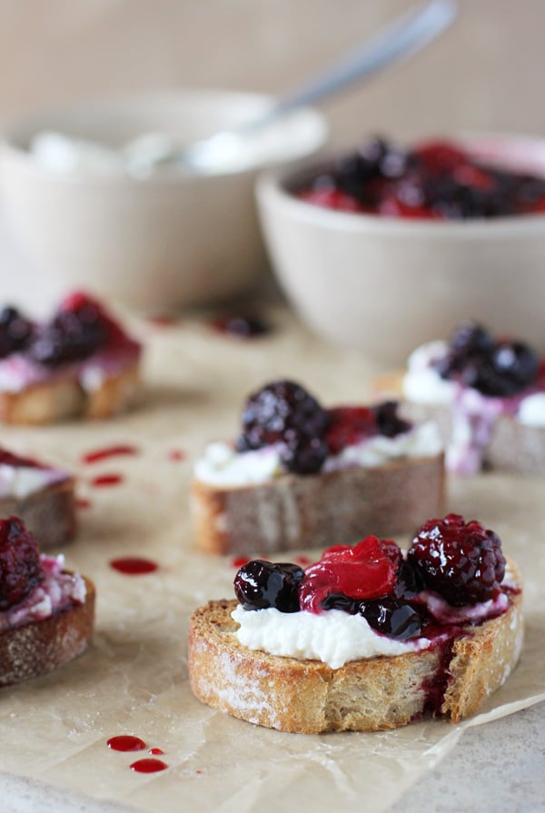 Several Berry Crostini on parchment paper with bowls in the background.