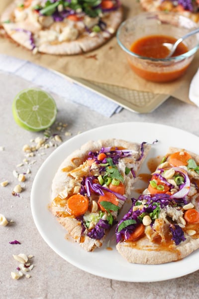 A Thai Chicken Pita Pizza sliced in half on a white plate.