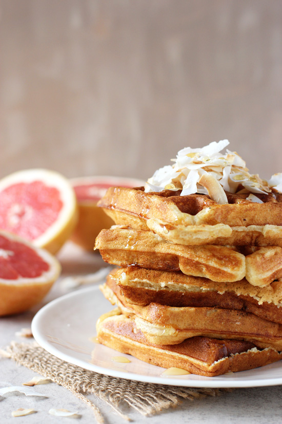Several Grapefruit Buttermilk Waffles stacked on a white plate.