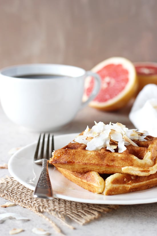 Two Grapefruit Waffles on a white plate with a cup of coffee in the background.