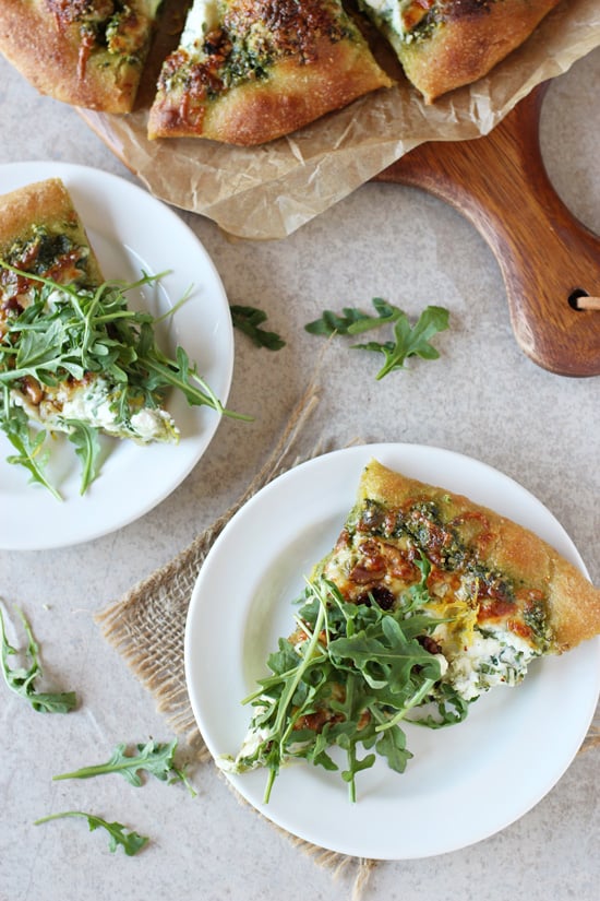 Two slices of Arugula Topped Pizza on white plates with the full pizza in the background.