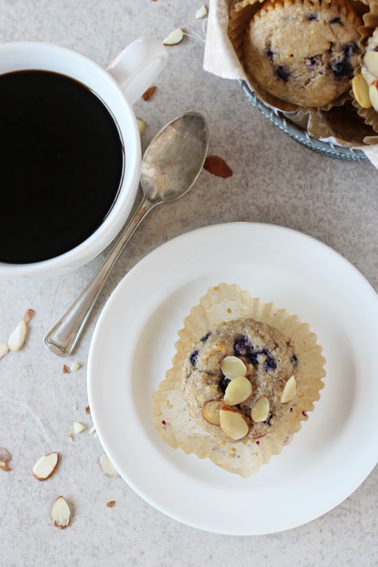 A white plate with a Whole Grain Blueberry Muffin and a cup of coffee.