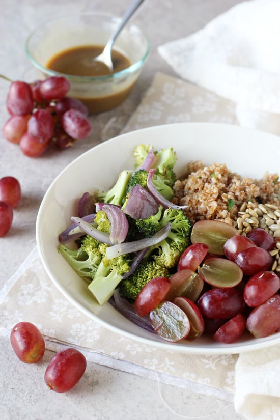 A white bowl filled with Broccoli Bulgur Salad with grapes scattered around.