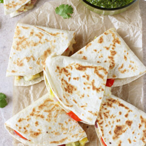 Recipe for weeknight sweet and salty thai vegetable quesadillas. Packed with red pepper, zucchini, cabbage and pineapple! Serve with a homemade cilantro pesto!