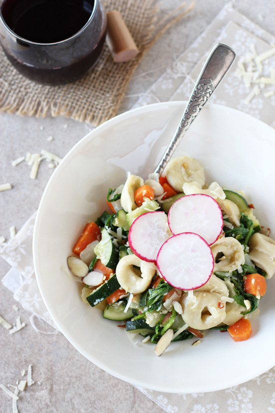 A white bowl filled with Veggie Tortellini skillet and a glass of wine.