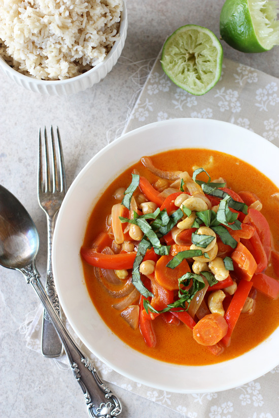 A white bowl filled with Vegan Thai Red Curry with rice in the background.