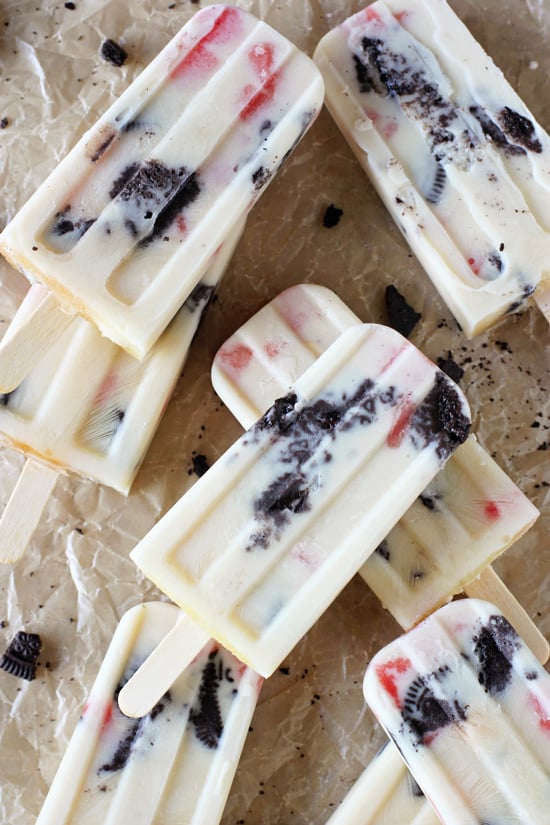 Several Creamy Watermelon Popsicles stacked on parchment paper.
