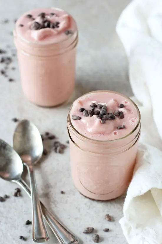 Two Watermelon Coconut Milkshakes in glass jars with spoons to the side.