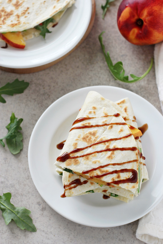 Two white plates filled with Peach Quesadillas with a peach to the side.