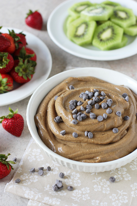A white bowl filled with Healthier Chocolate Fruit Dip with fruit in the background.