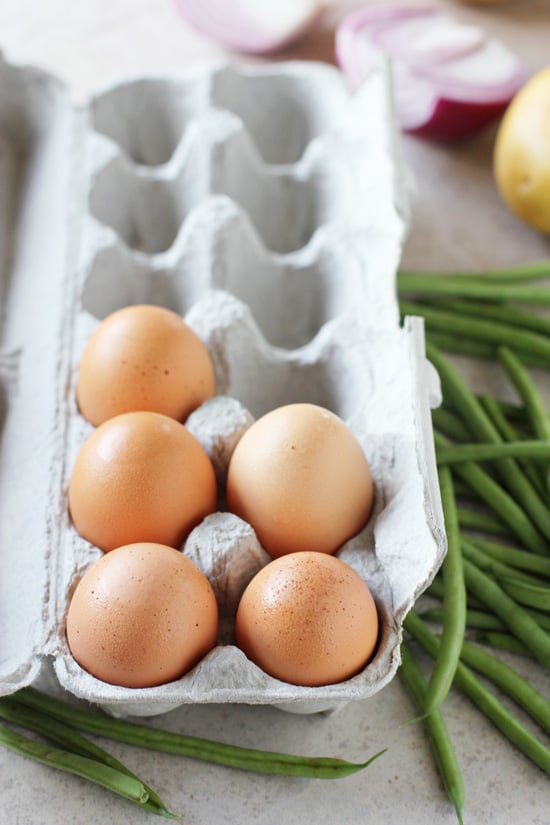 An opened egg carton and fresh green beans to the side.