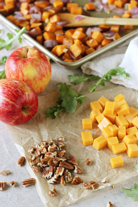A tray of roasted veggies, chopped pecans, cubed cheddar and two apples.