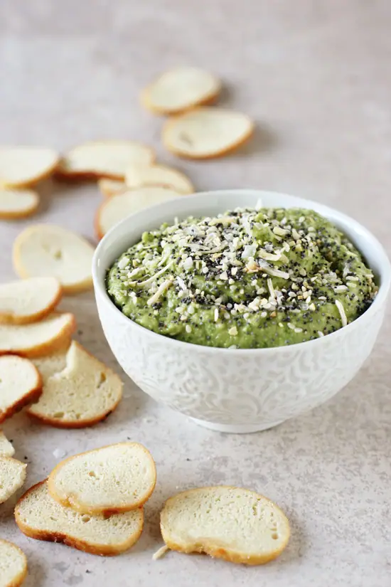 A white bowl filled with Everything Spinach Chickpea Dip with bagel chips to the side.