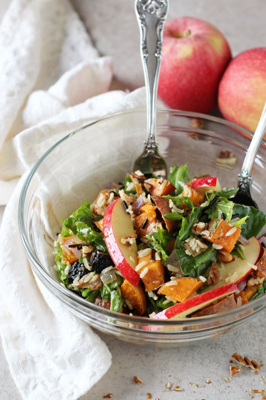 A glass mixing bowl filled with Harvest Salad with two serving spoons in the dish.