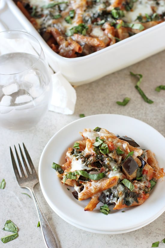 A white plate filled with Kale and Eggplant Pasta with a baking dish in the background.