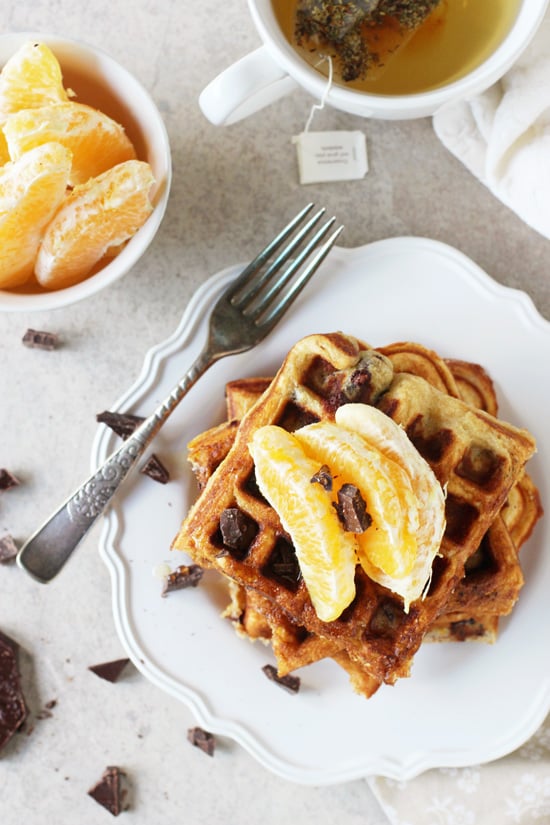 Several Orange and Dark Chocolate Waffles stacked on a white plate with a cup of tea to the side.