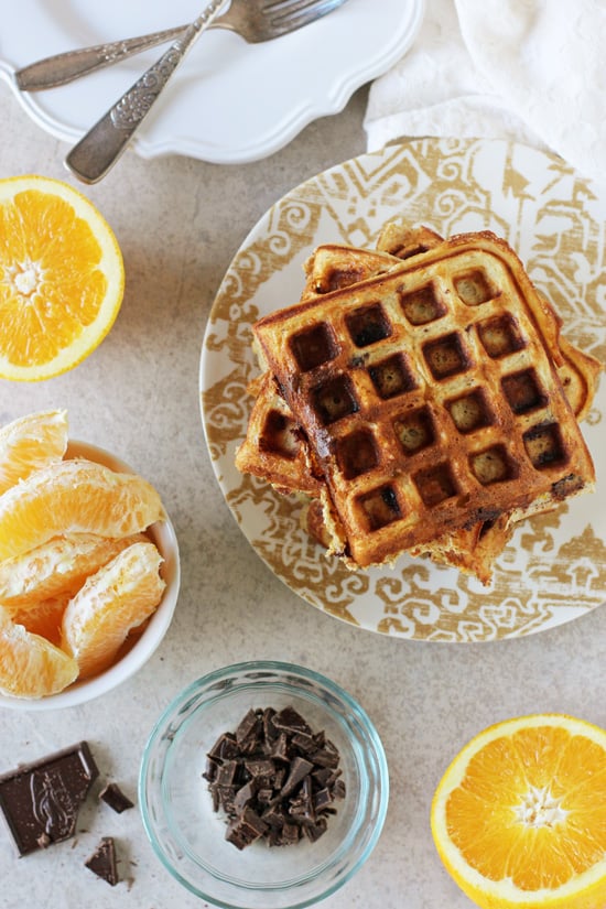 A plate with Orange Chocolate Waffles and bowls of orange slices and chopped chocolate.