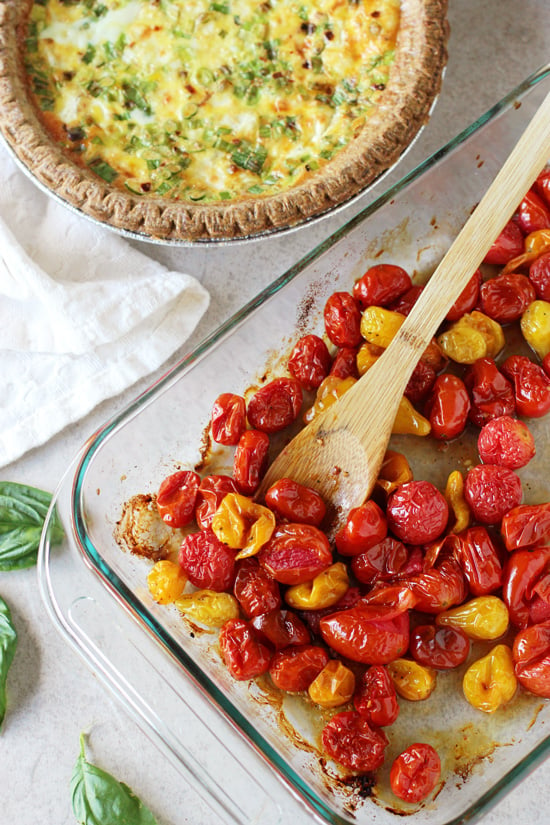 A tray of roasted tomatoes with a baked Goat Cheese Tomato Quiche to the side.
