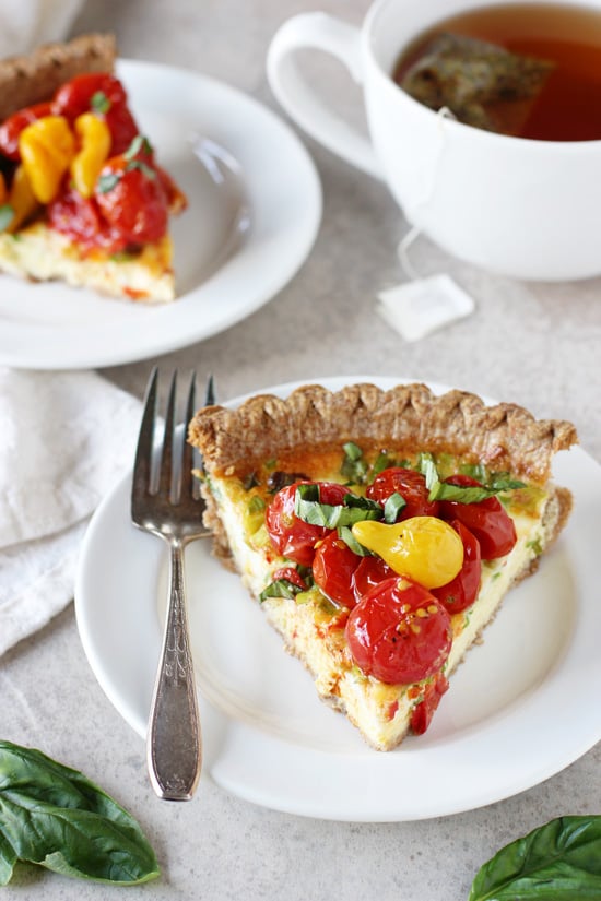 A slice of Roasted Tomato Quiche with a cup of tea in the background.