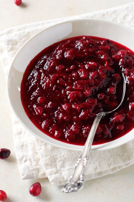 A white bowl filled with Vanilla Cranberry Sauce with a spoon in the dish.