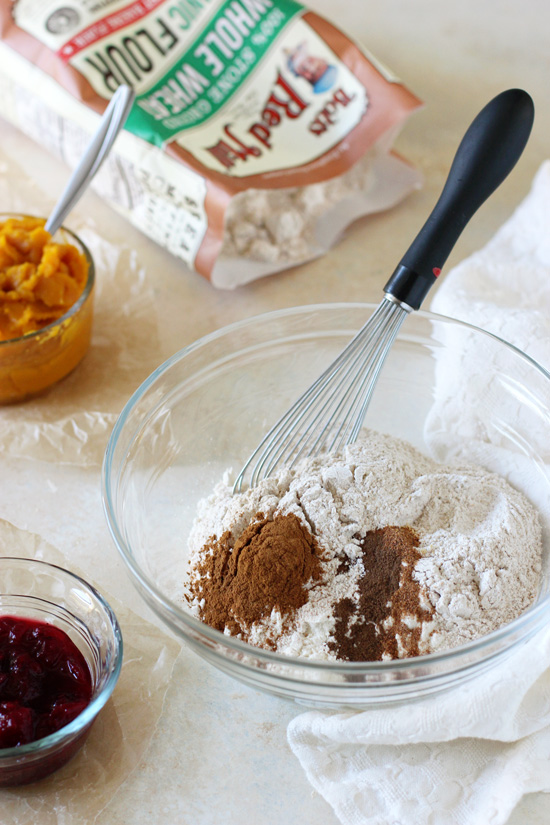 A glass bowl filled with flour and spices, and small bowls filled with pumpkin puree and cranberry sauce.
