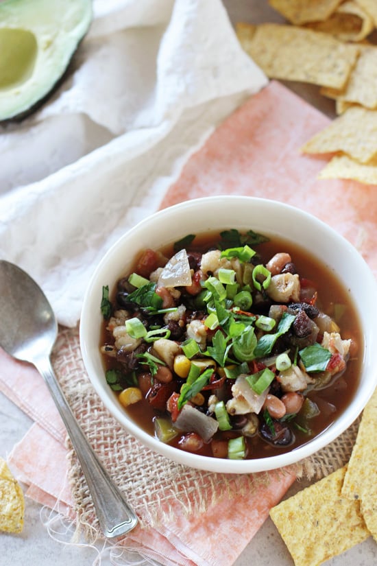 A white bowl filled with Slow Cooker Vegetarian Tortilla Soup with chips scattered around.