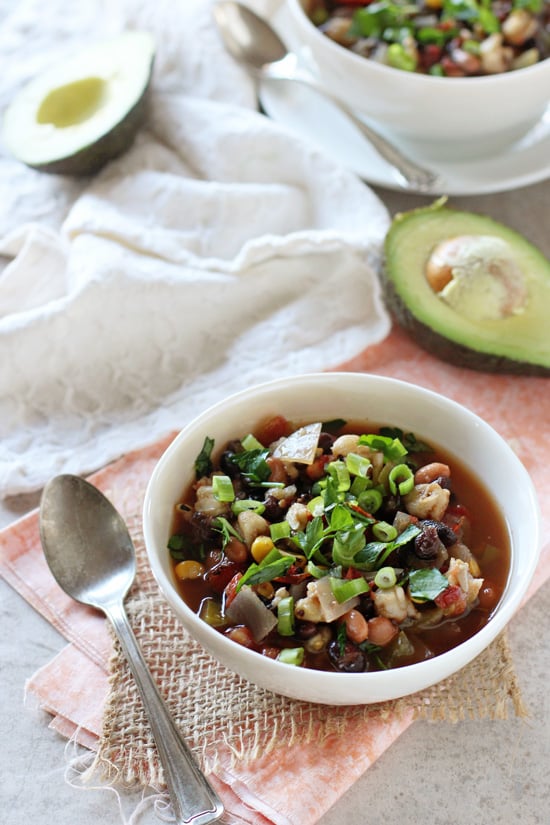 Two bowls filled with Crockpot Vegetarian Tortilla Soup with avocado halves to the side.
