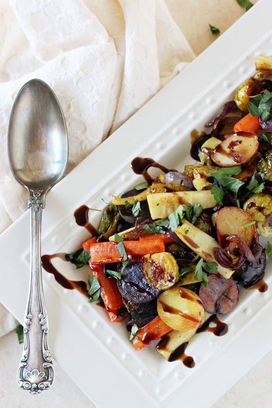 A white serving platter with Honey Balsamic Roasted Vegetables with a spoon to the side.