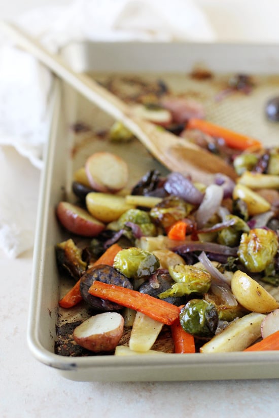 A baking sheet with Honey Balsamic Vegetables with a wooden spoon in the pan.