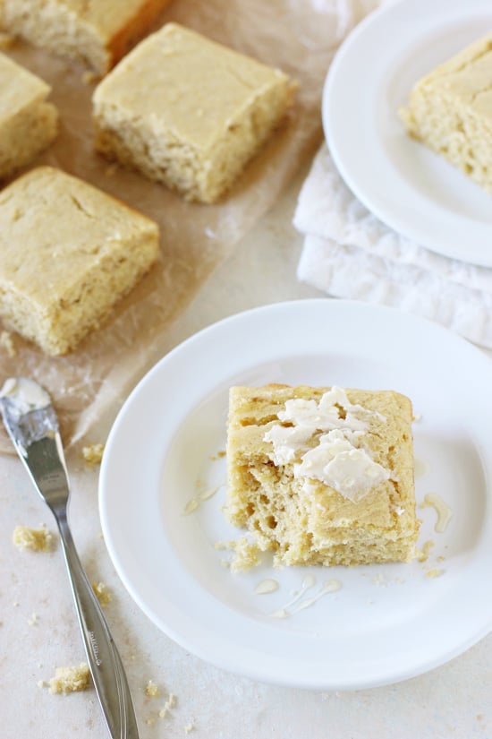 A piece of Fluffy Cornbread slathered with butter on a white plate.