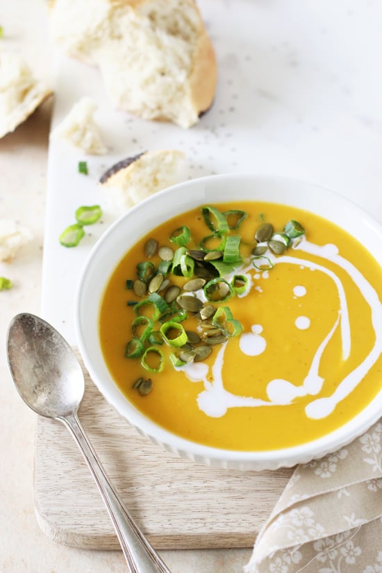 A white bowl filled with Roasted Garlic Butternut Squash Soup with bread in the background.