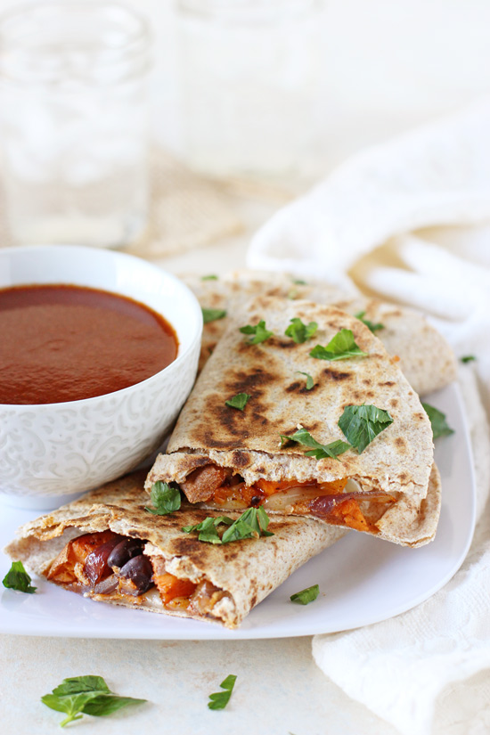 Several Roasted Vegetable Quesadillas on a white plate with enchilada dipping sauce.