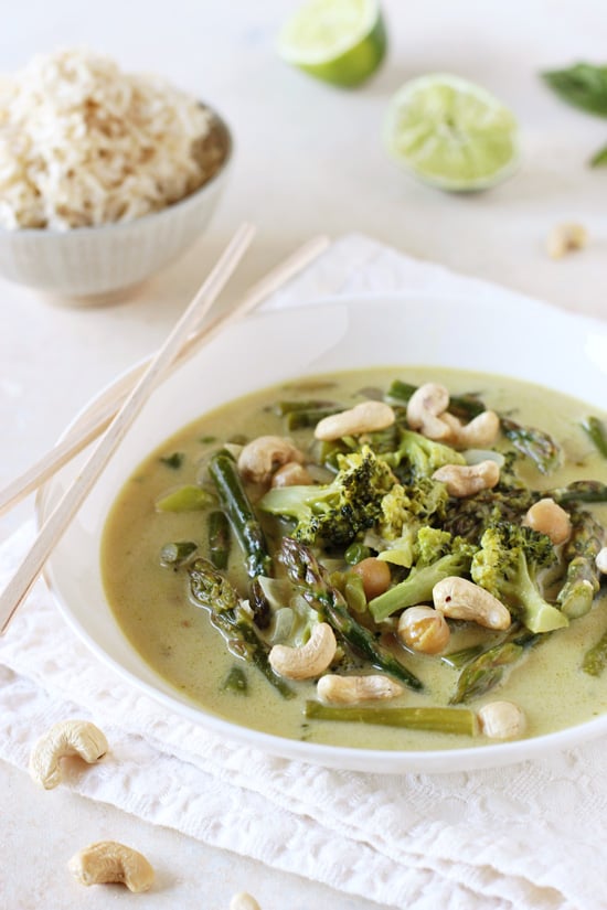 A white bowl filled with Vegetarian Thai Green Curry with a bowl of rice in the background.