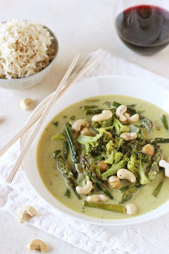 A white bowl filled with Vegan Thai Green Curry with a bowl of rice and wine in the background.